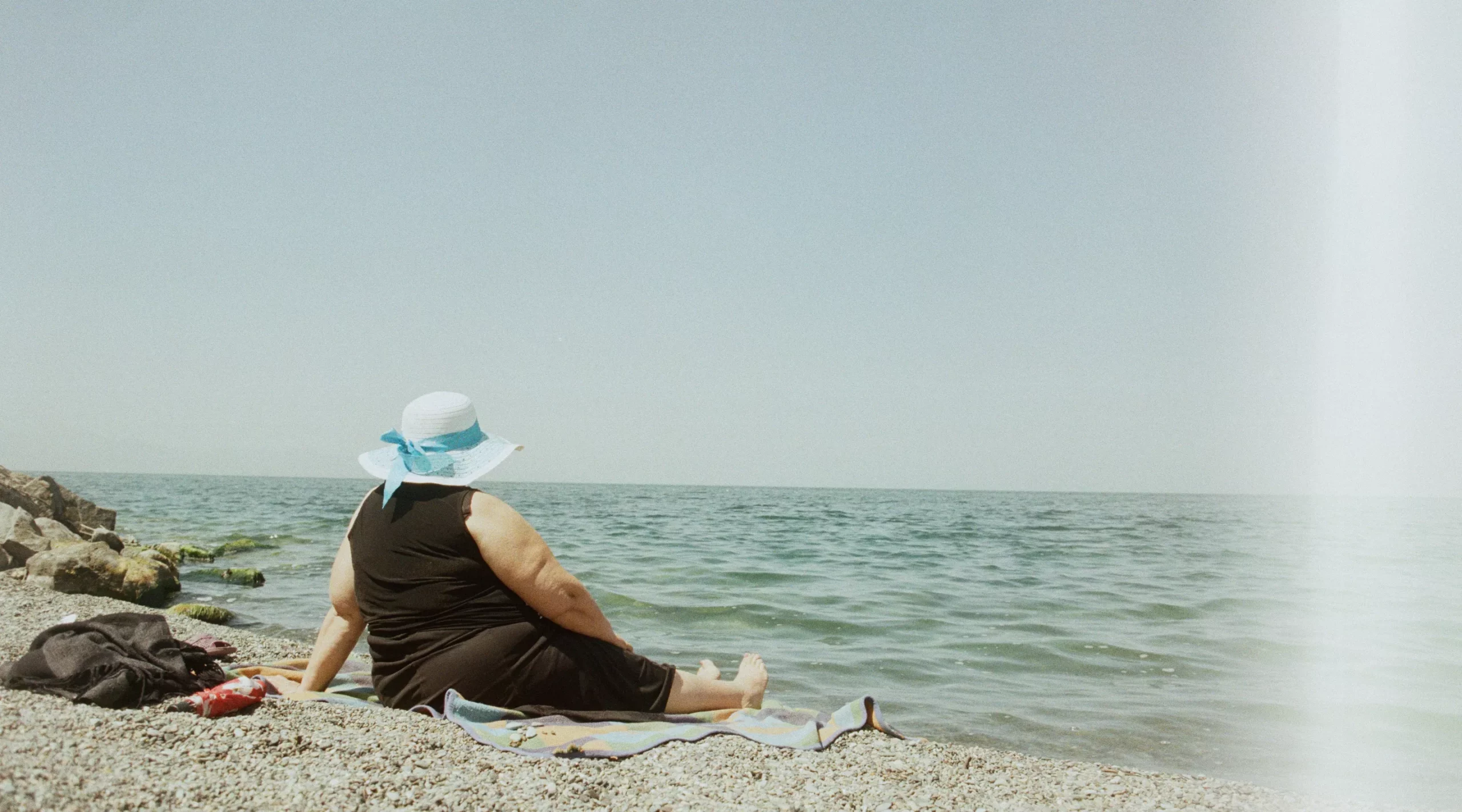 Femme assise sur une plage de galets avec un chapeau sur la tête