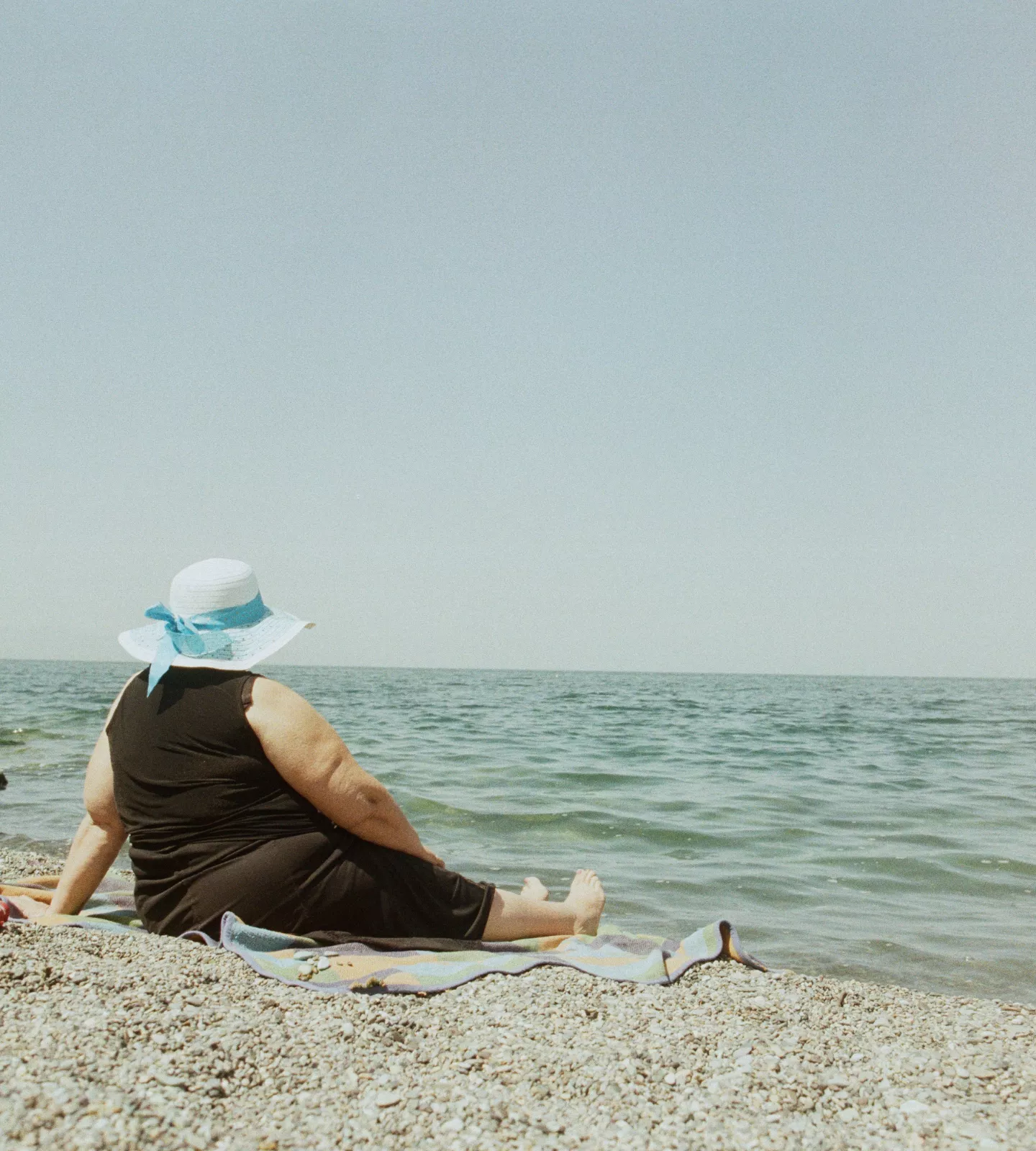 Femme assise sur une plage de galets avec un chapeau sur la tête